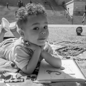 boy laying on blanket with coloring book outside