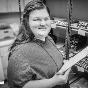 young woman holds a clipboard while working in a screen printing shop