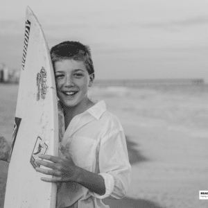 boy stands on the beach with is surfboard