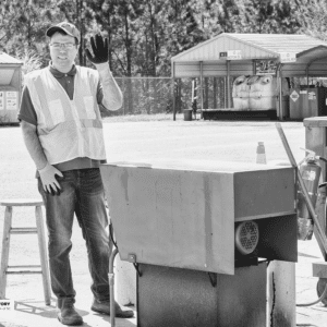 young man waves next to a trash compactor