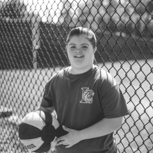 girl stands by a fence with her basketball