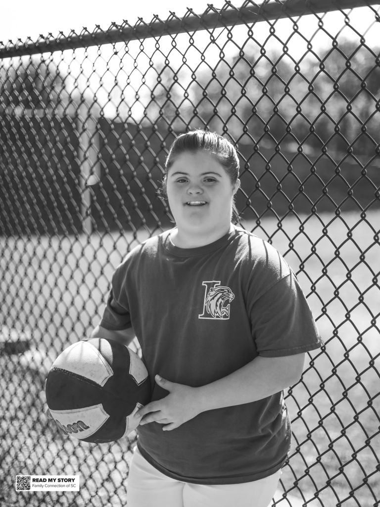 girl stands by a fence with her basketball