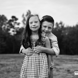 sister and brother stand together in a field