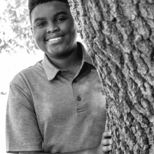 boy stands behind a tree