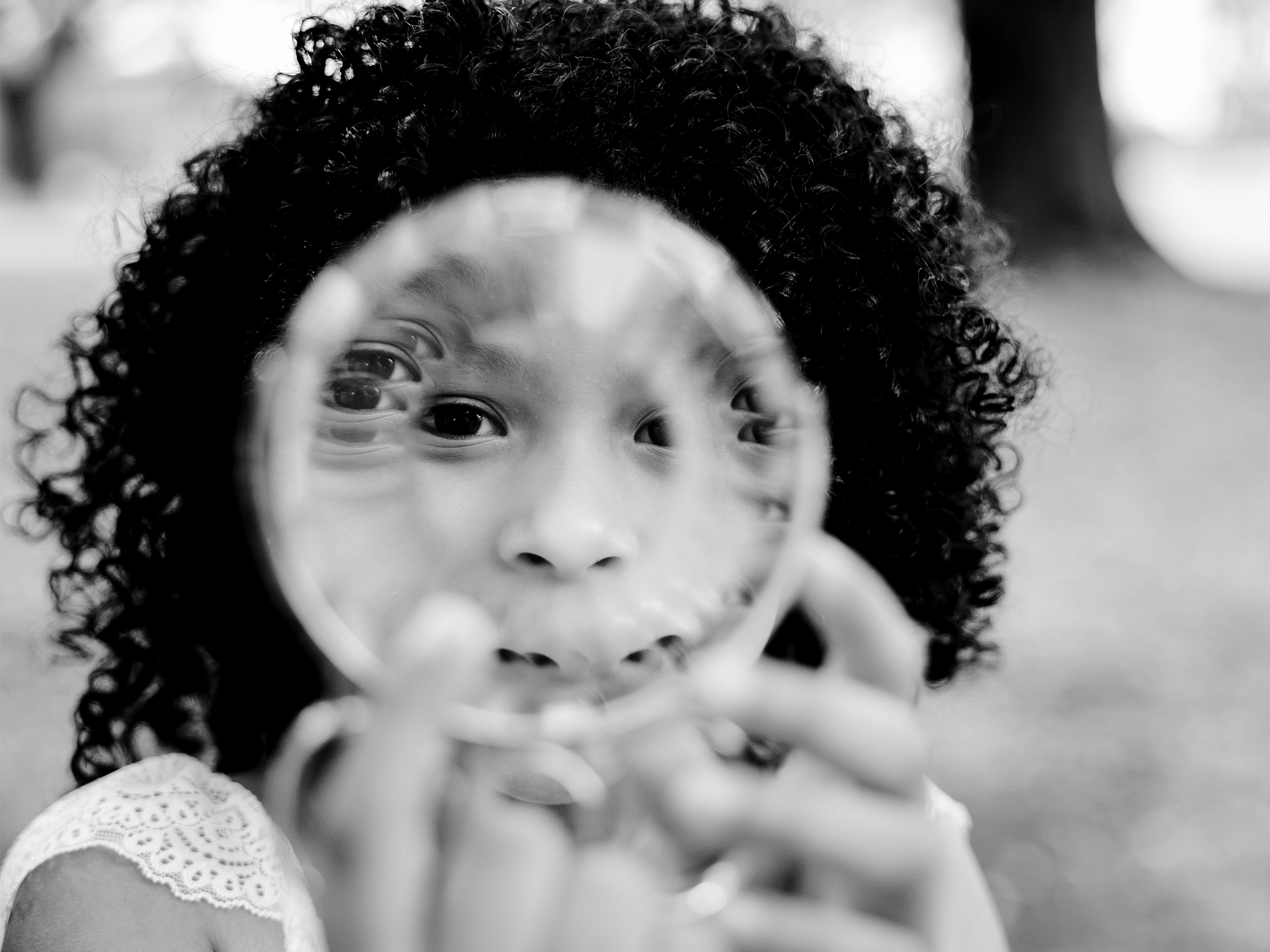 Black and white photo of female child looking through spiral ring