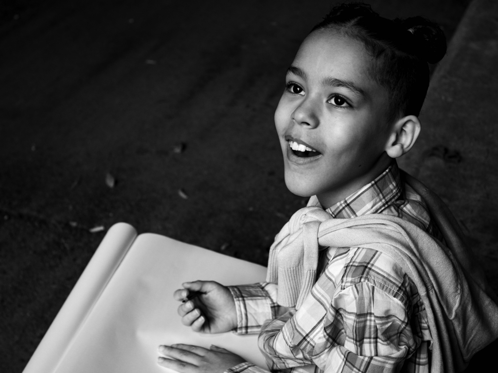 Black and white photo of female child smiling looking up and holding paper