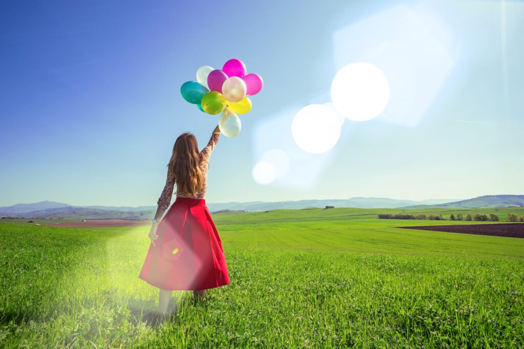woman with red dress holding balloons in a field