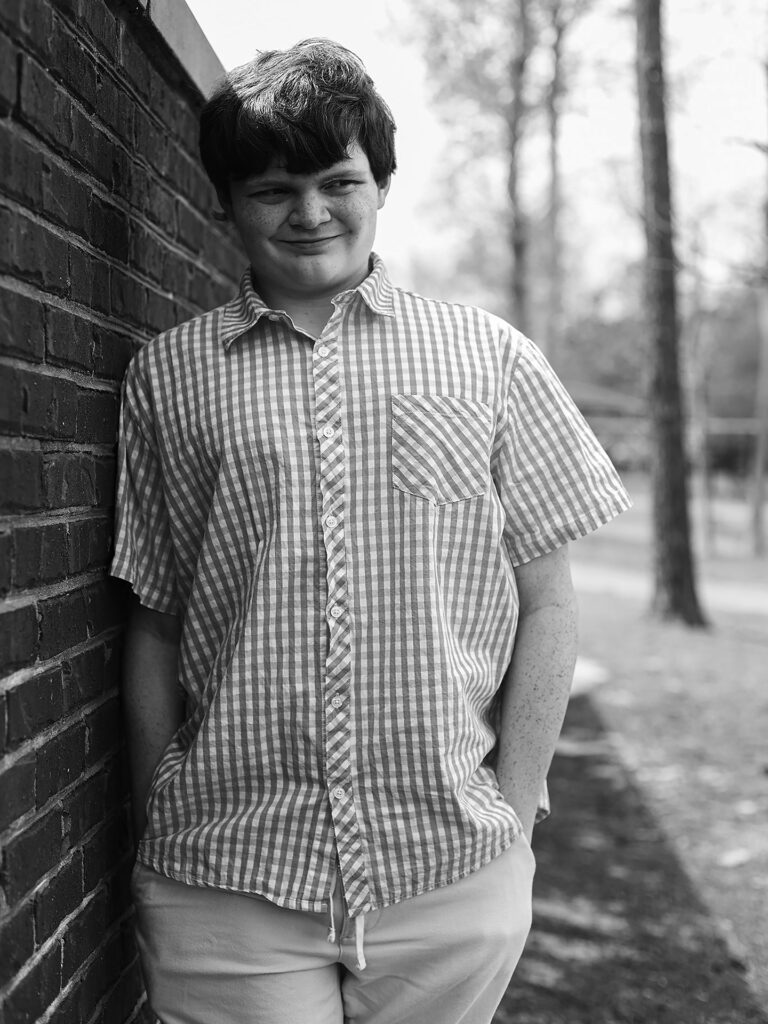 young man smiles leaning on a brick wall