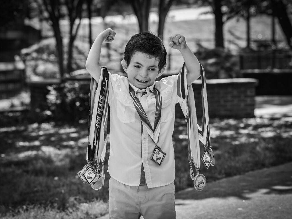 young boy holds up his arms full of medels