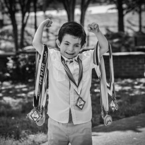 young boy holds up his arms full of medels