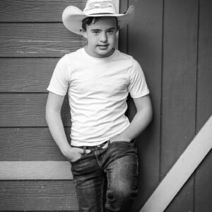young man in cowboy hat stands against a barn