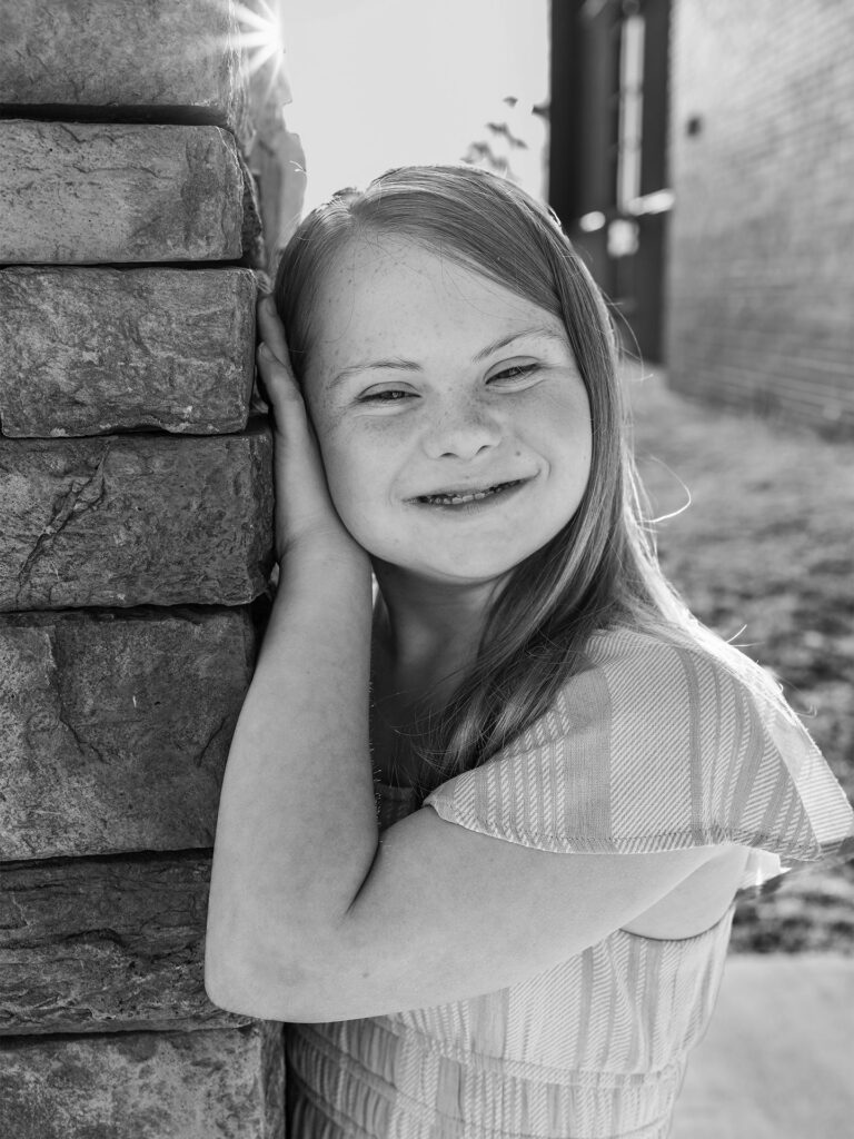 girl smiles leaning on a stone wall with the sun behind her