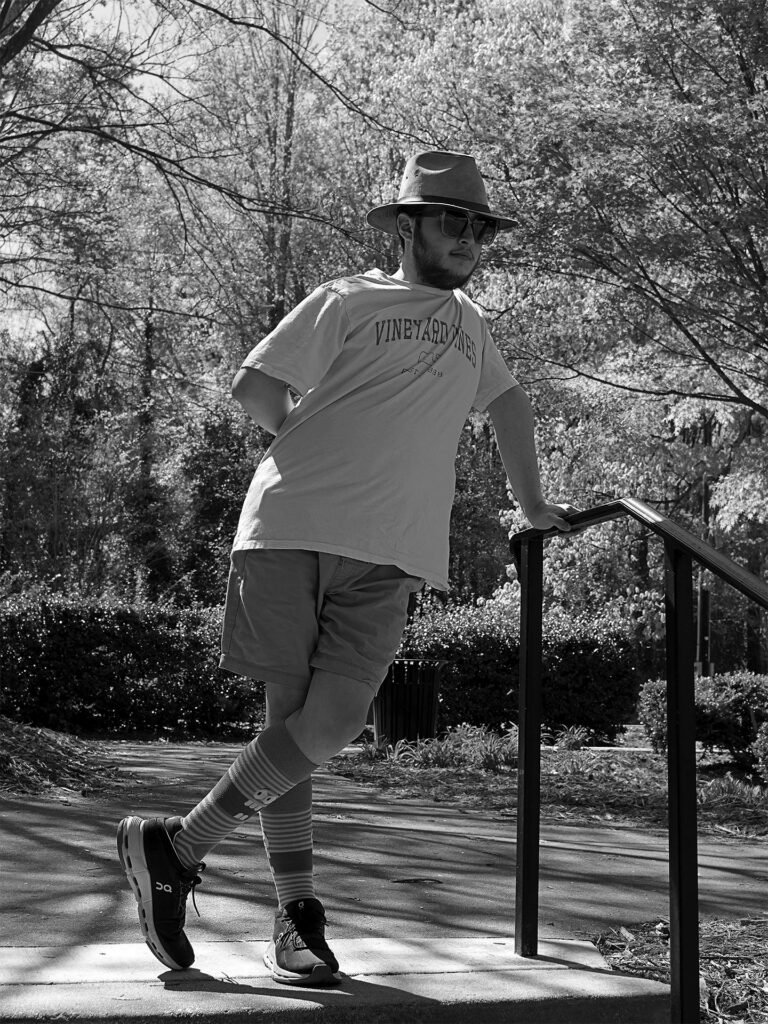 young man in hat and glasses leans against a railing